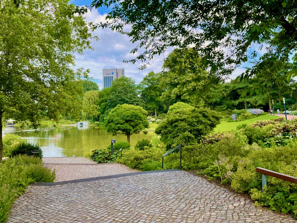 Sumérgete en un pintoresco trozo de naturaleza en el centro de Hamburgo, eso es posible si te calzas las zapatillas de correr y exploras la encantadora ruta para correr a través de Planten un Blomen. El extenso parque es una verdadera joya de la ciudad y ofrece un entorno idílico para hacer jogging o caminar relajados en medio de magníficas plantas, coloridos macizos de flores e impresionantes paisajes acuáticos. Los senderos bien cuidados pasan por numerosas atracciones que hacen que correr sea una experiencia inolvidable. Descubra el jardín de rosas con sus más de 300 variedades de rosas, el jardín japonés, que irradia un estilo del Lejano Oriente, o el impresionante órgano de luz de agua, que crea una atmósfera atmosférica, especialmente en las horas de la noche. Foto: Sascha Tegtmeyer