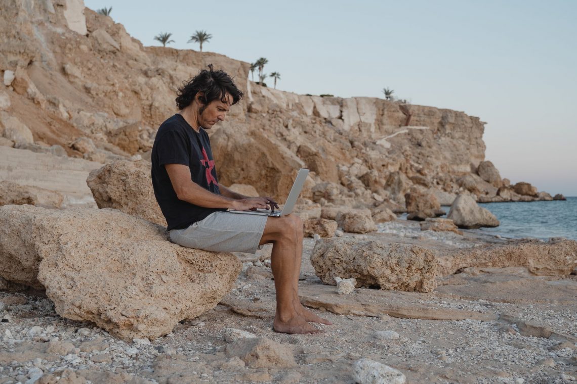 man sitting on a rock while using a laptop